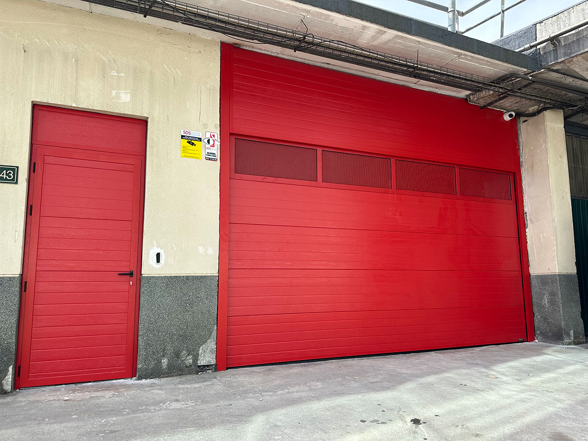Puerta seccional industrial semi-guillotina, con motor, con panel superior ventilado y con una puerta peatonal - Puertas Merino Gipuzkoa